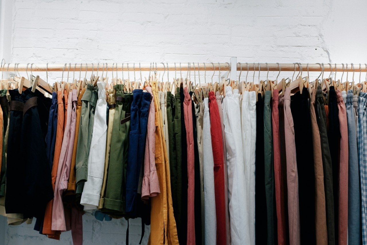A colourful assortment of clothes on hangers along a wooden rail.