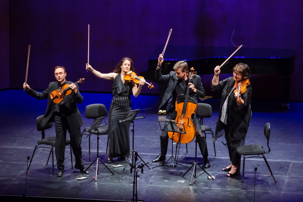 Four musicians on stage playing violins.