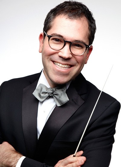 Man wearing a suit and bowtie, holding a conductor's baton