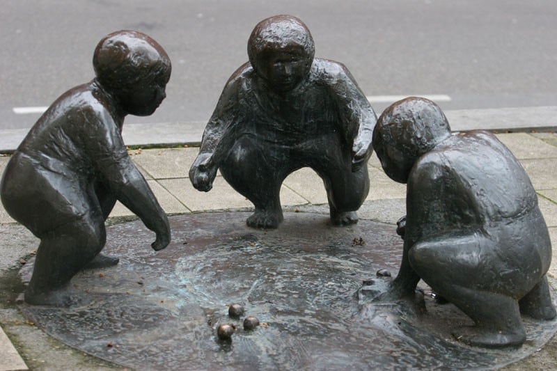 Three bronze figures of children play with marbles