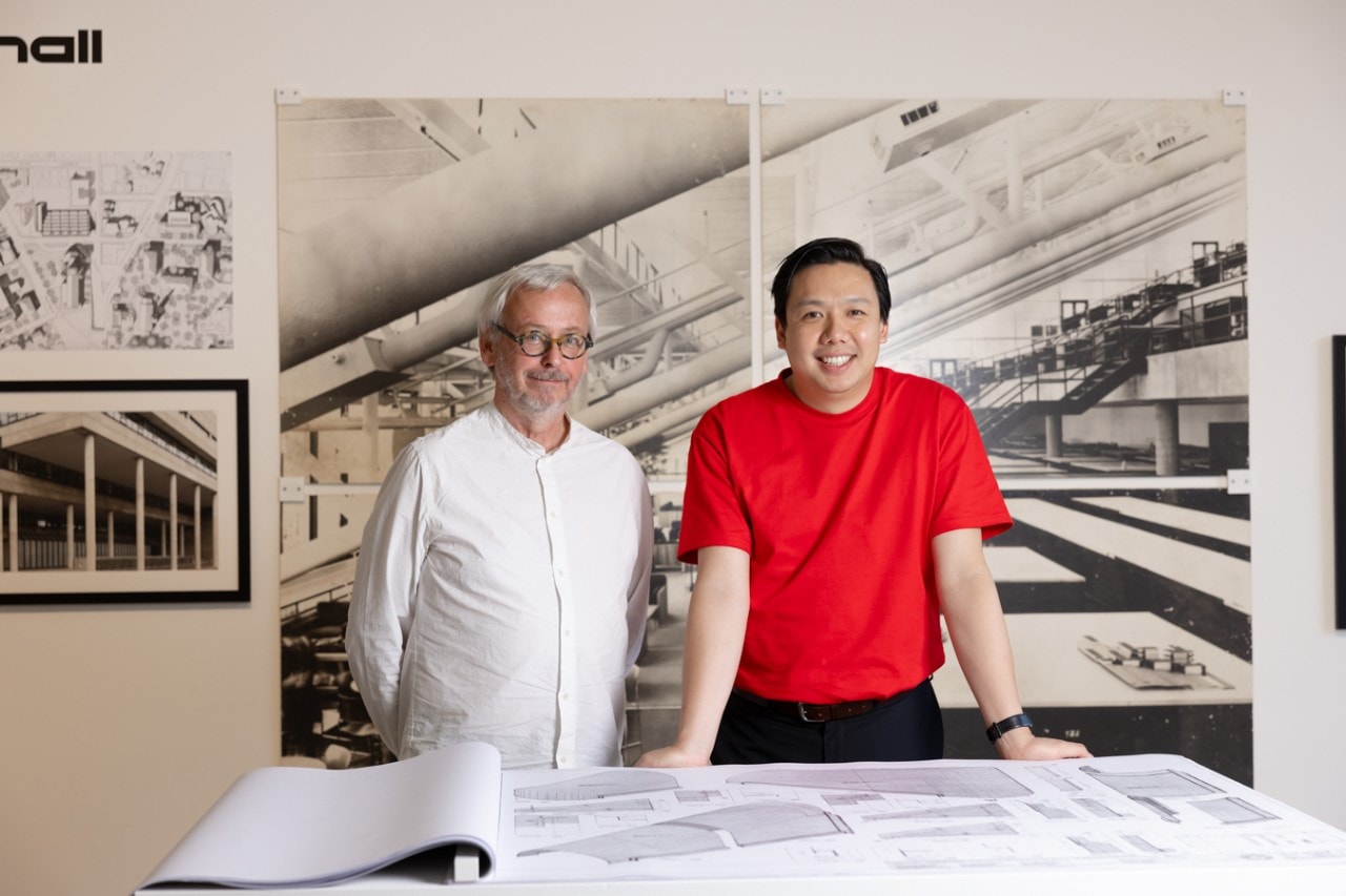 Two men standing in front of a wal displaying architectural drawings and photos