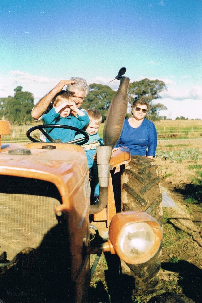 Guy Boncardo's father on a tractor in the market garden with his grandchildren on his lap. His mother stands in the background.