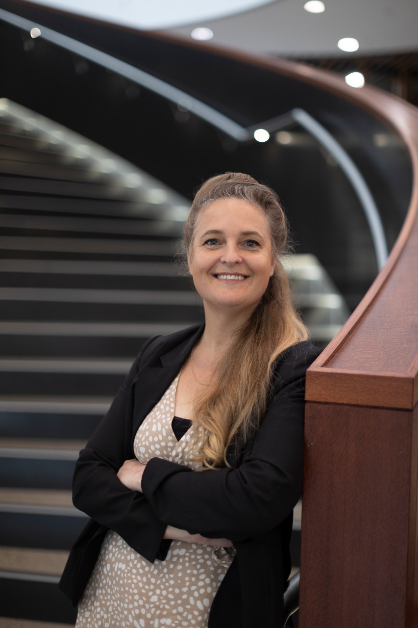 Henia Colinard standing with her arms folded, leaning against the spiral steps of the Business School.