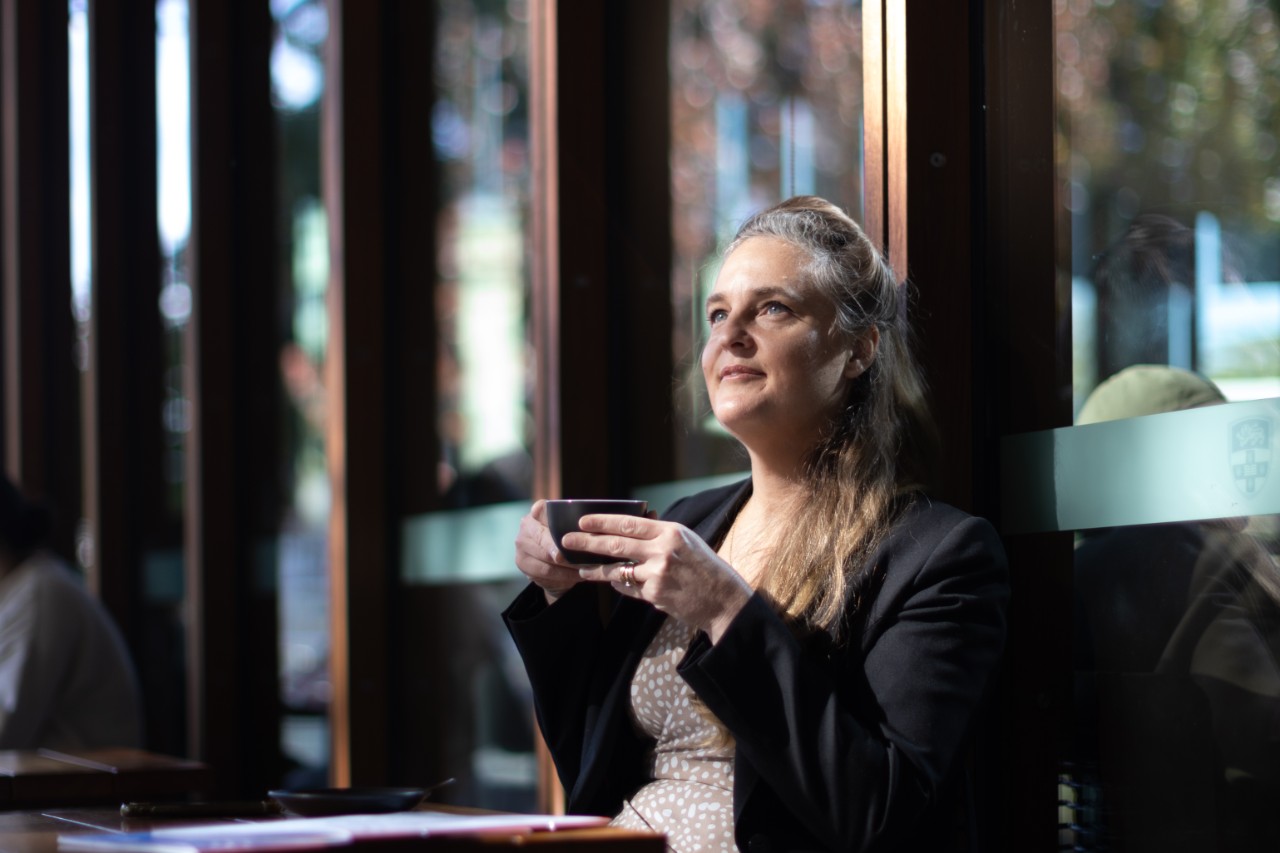 Henia Colinard seated, holding a cup of coffee outside the Business School.