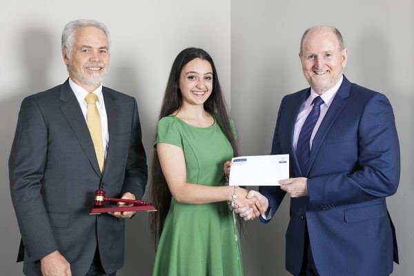 Piadora shaking hands with John Bateman and Michael Battersby while smiling and holding an award,