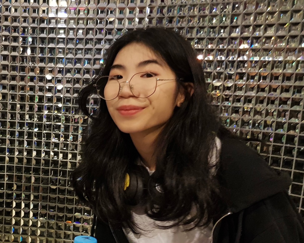A girl in front of a shiny tiled wall smiling