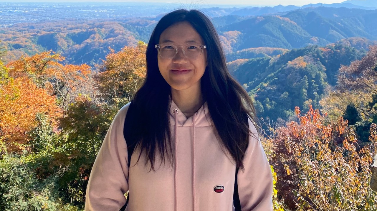 A girl stood in front of scenic nature, smiling