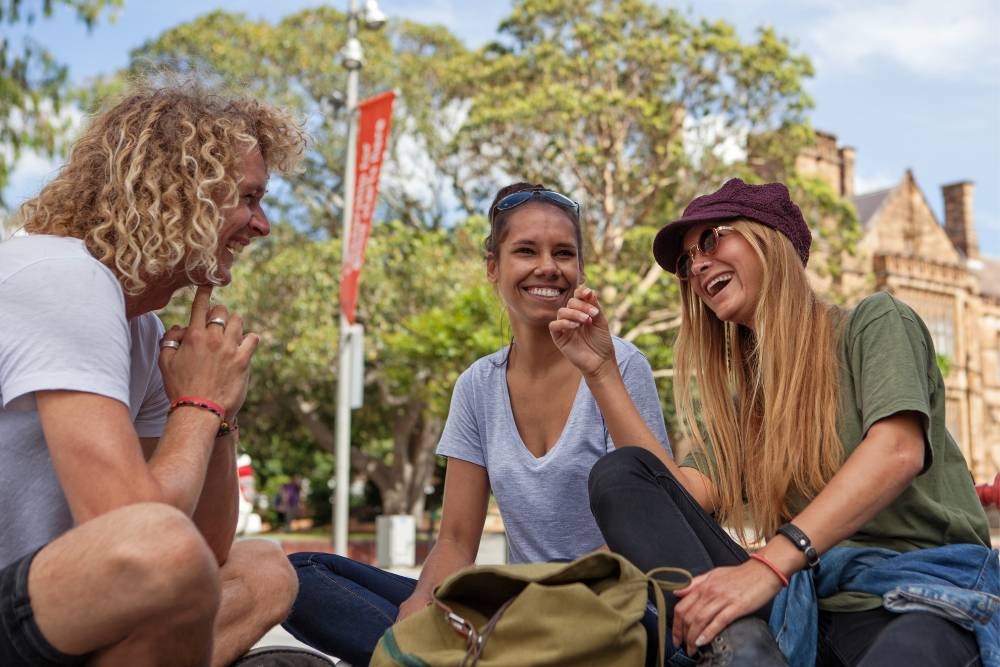 Two women and a man sit outside the Quadrangle talking and laughing