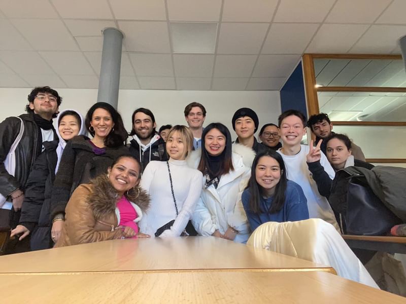 Robert surrounded by classmates with a desk in front smiling at the camera