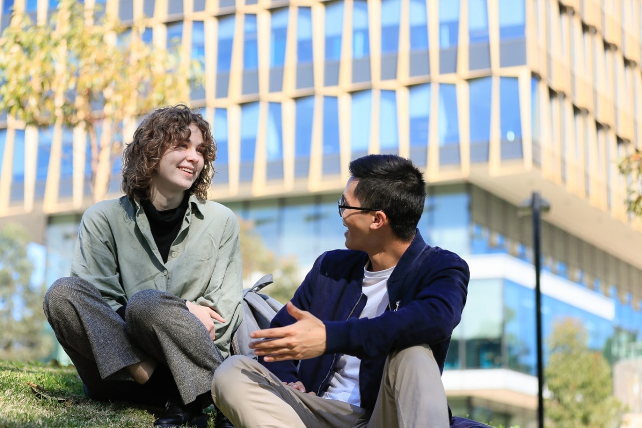 Two students talking to each other on a grassy hill.