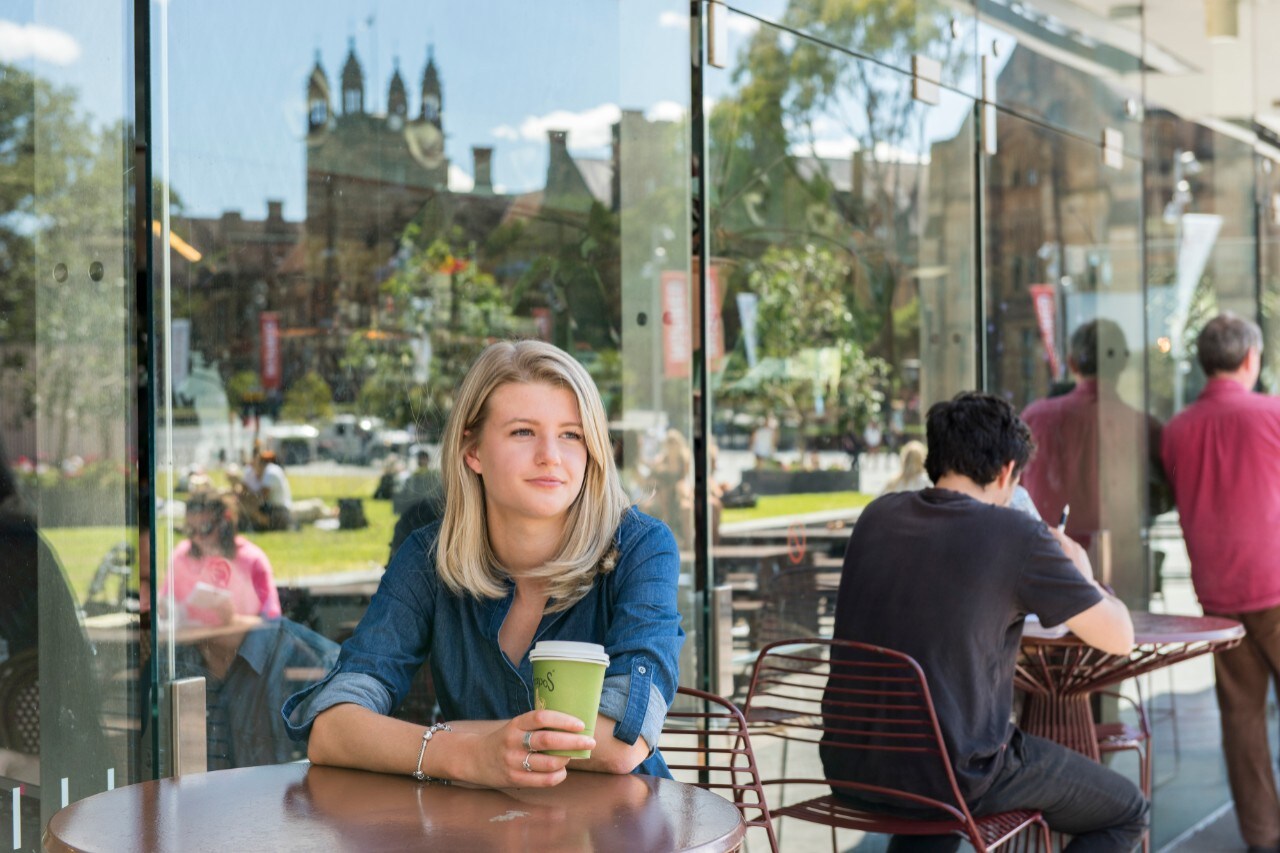 Photo of a student drinking coffee on a sunny day on Eastern Avenue