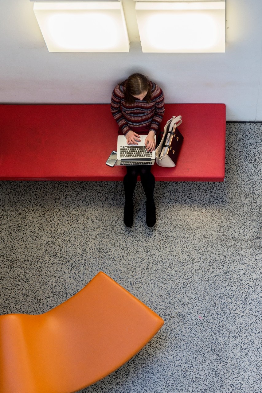 Aerial view of female student sitting on a bench using a laptop