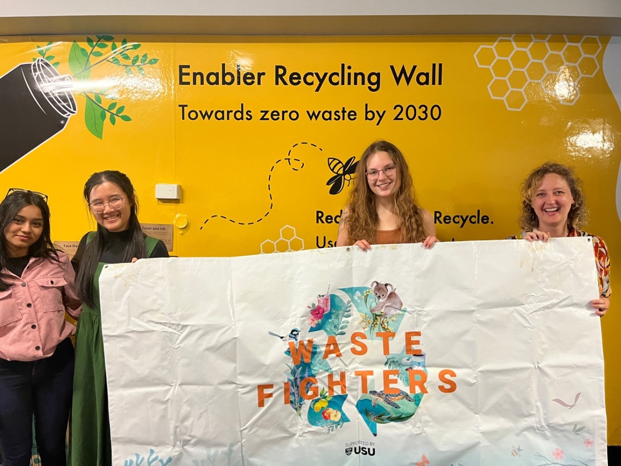 Students and staff posing for a photograph against the Enabler Wall in Wentworth Building holding up a banner that says: "Waste Fighters".