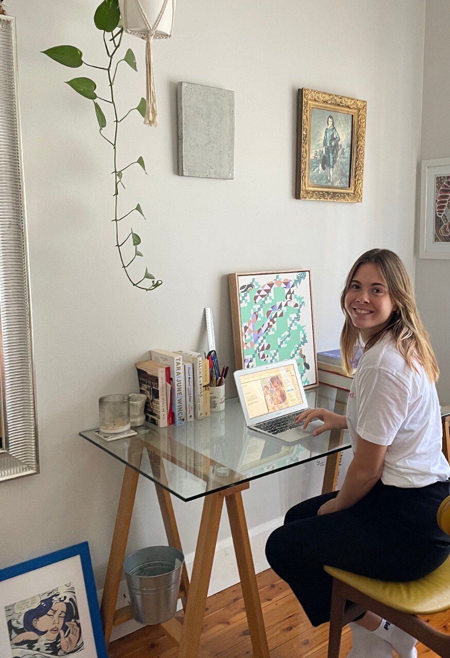 Chloe Mossissey sitting in her study space, surrounded by paintings and plants