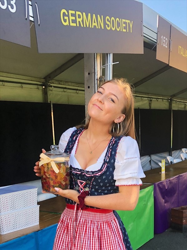 Indigo dressed in a traditional Bavarian dress holding a jar of gummy bears as she represents the German Society at the University's welcome week