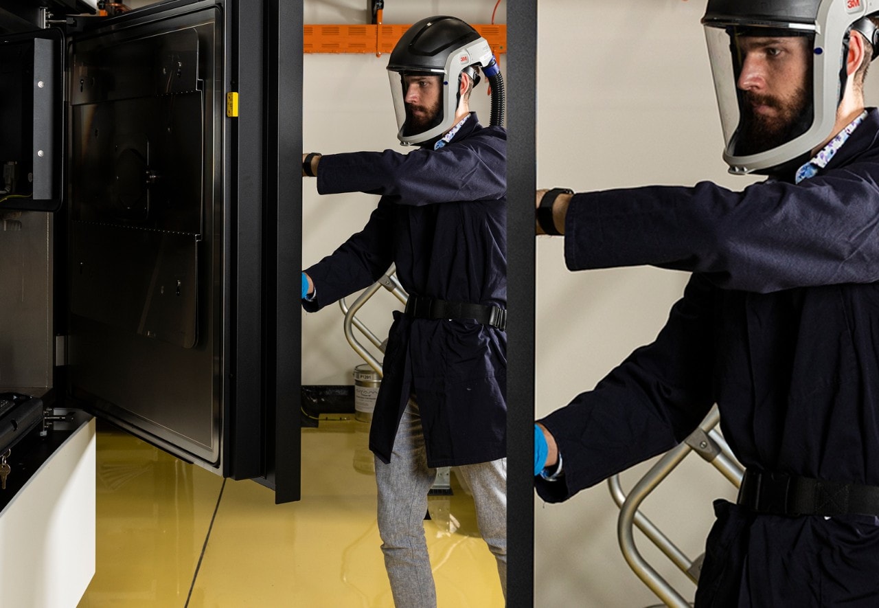 Person wearing protective clothing and a face shield in a lab setting closing a heavy cabinet door
