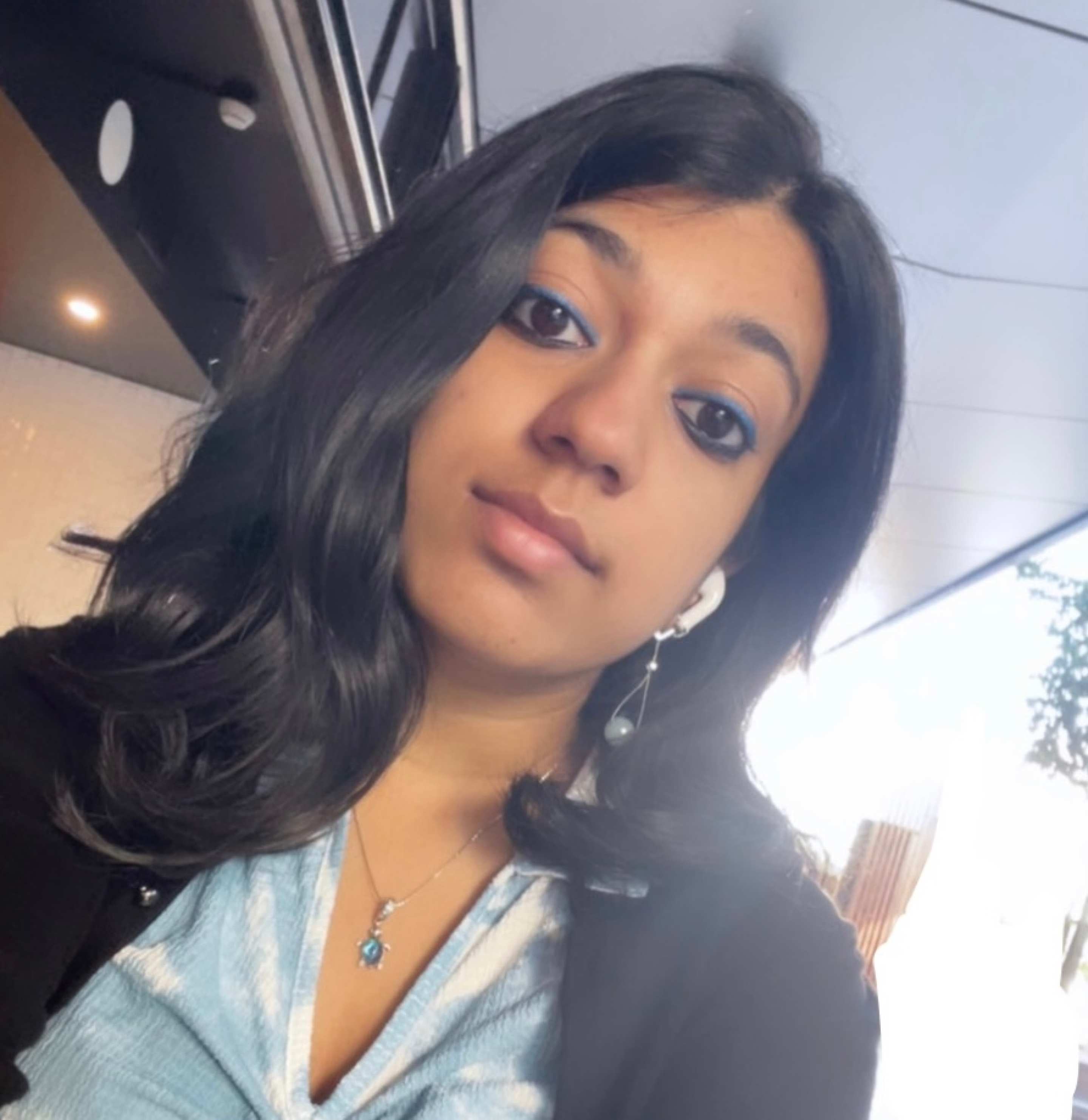 A headshot of Smrithi. Smrithi is wearing a light blue shirt with a black overcoat and has long, black hair. 
