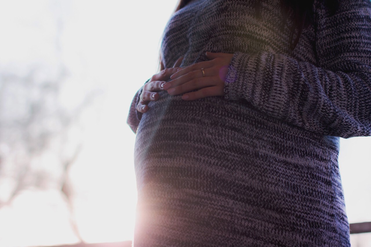 Woman in grey sweater with hands on pregnant belly