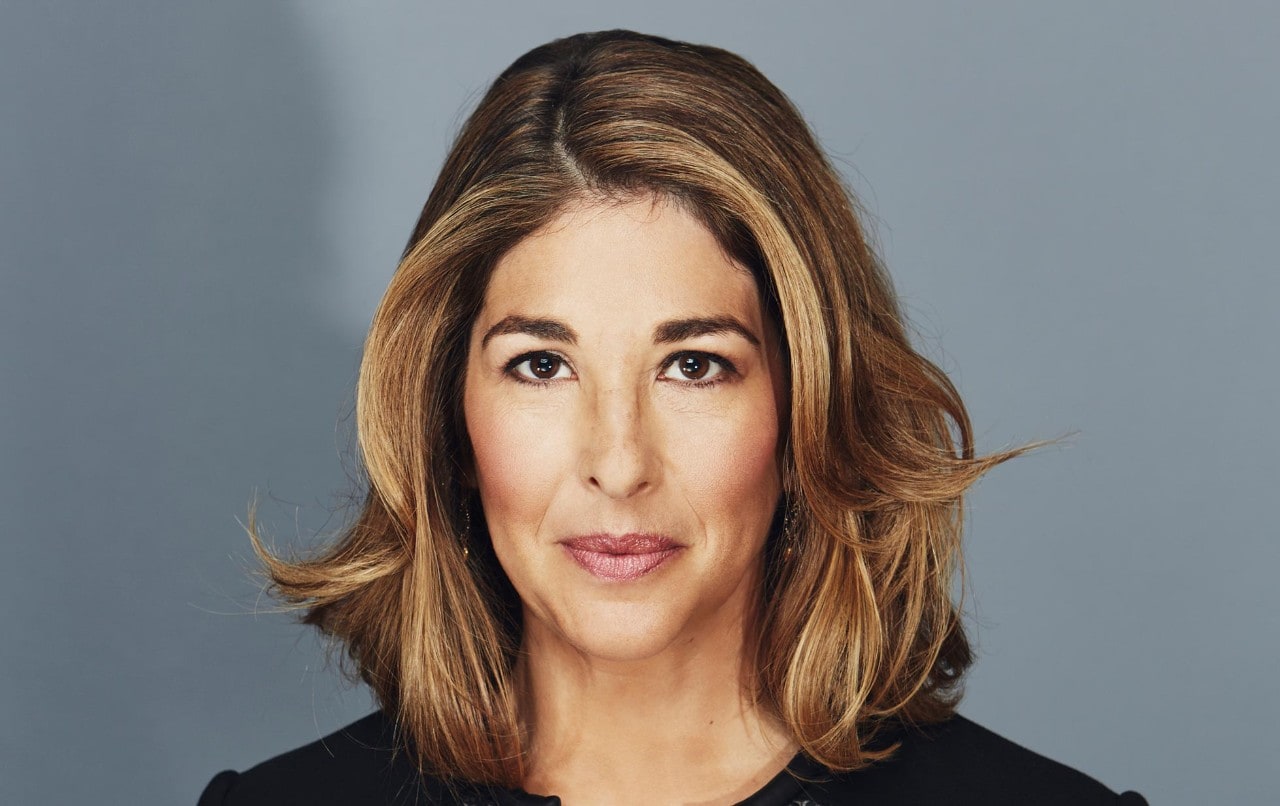A photograph of Naomi Klein holding spectacles. 