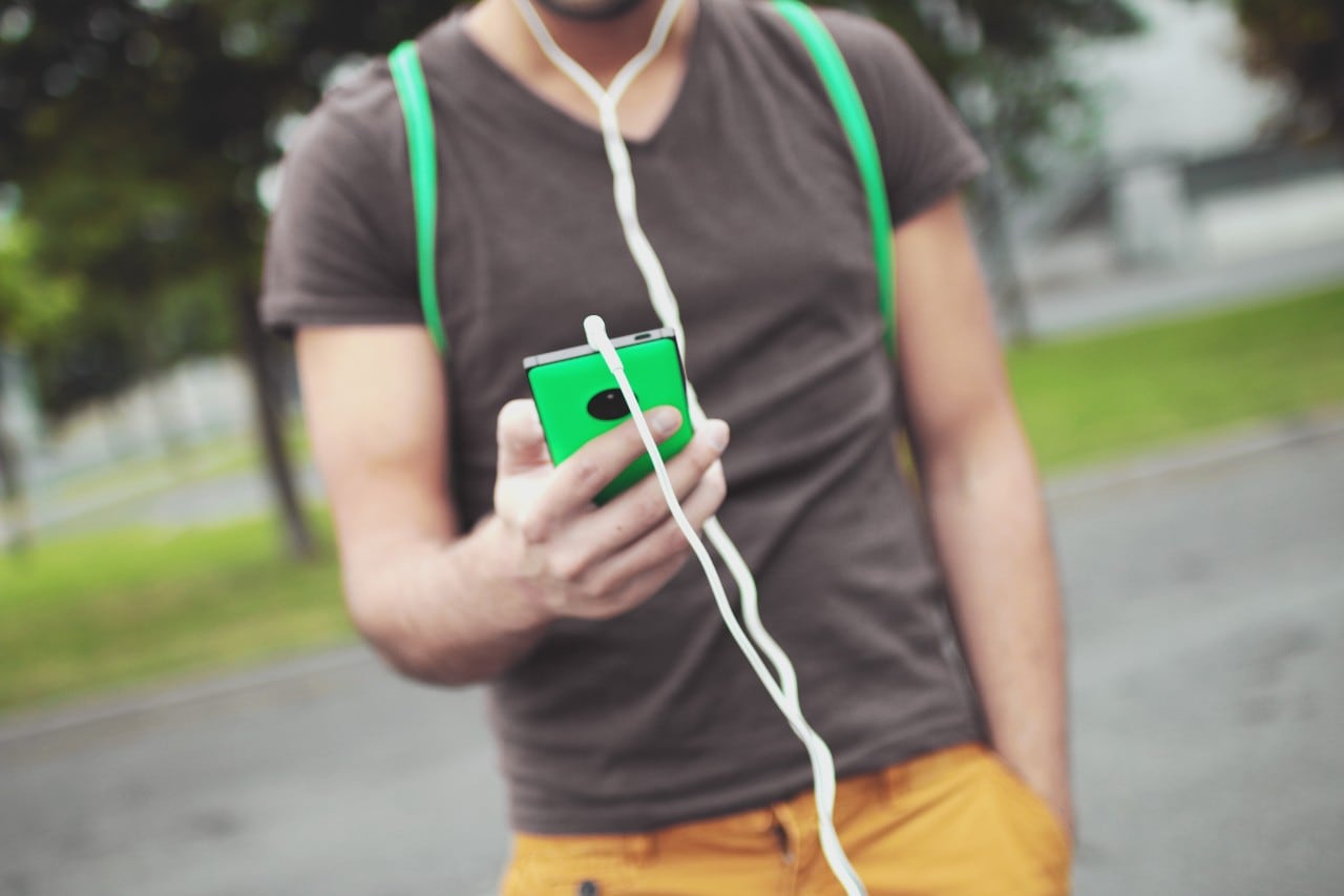 Torso of student holding phone with green case and headphones plugged in