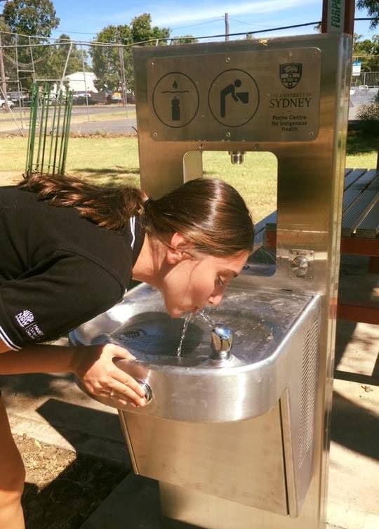 Photo of a woman drinking from a water fountain. 