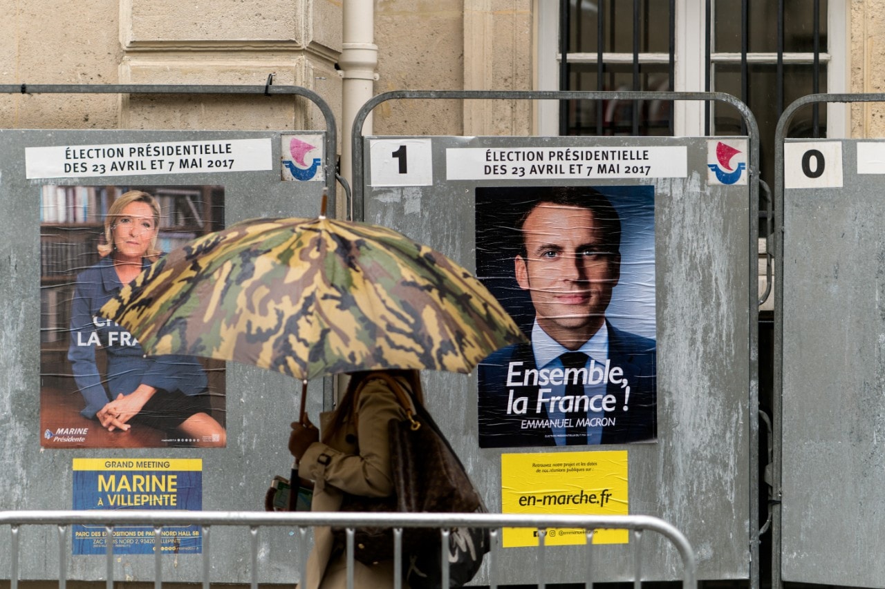 A woman with an umbrella walks past French presidential election posters. Image: Lorie Shaull/Wikimedia Commons
