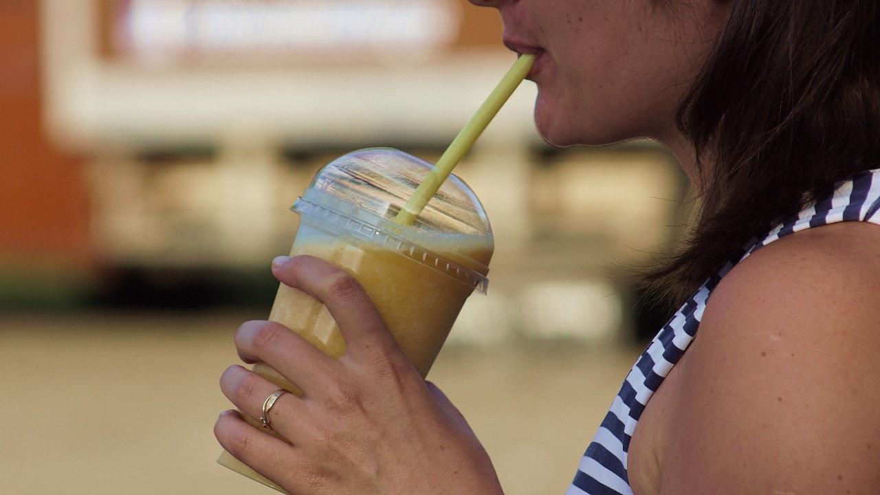 A person drinking from a plastic cup with a straw.