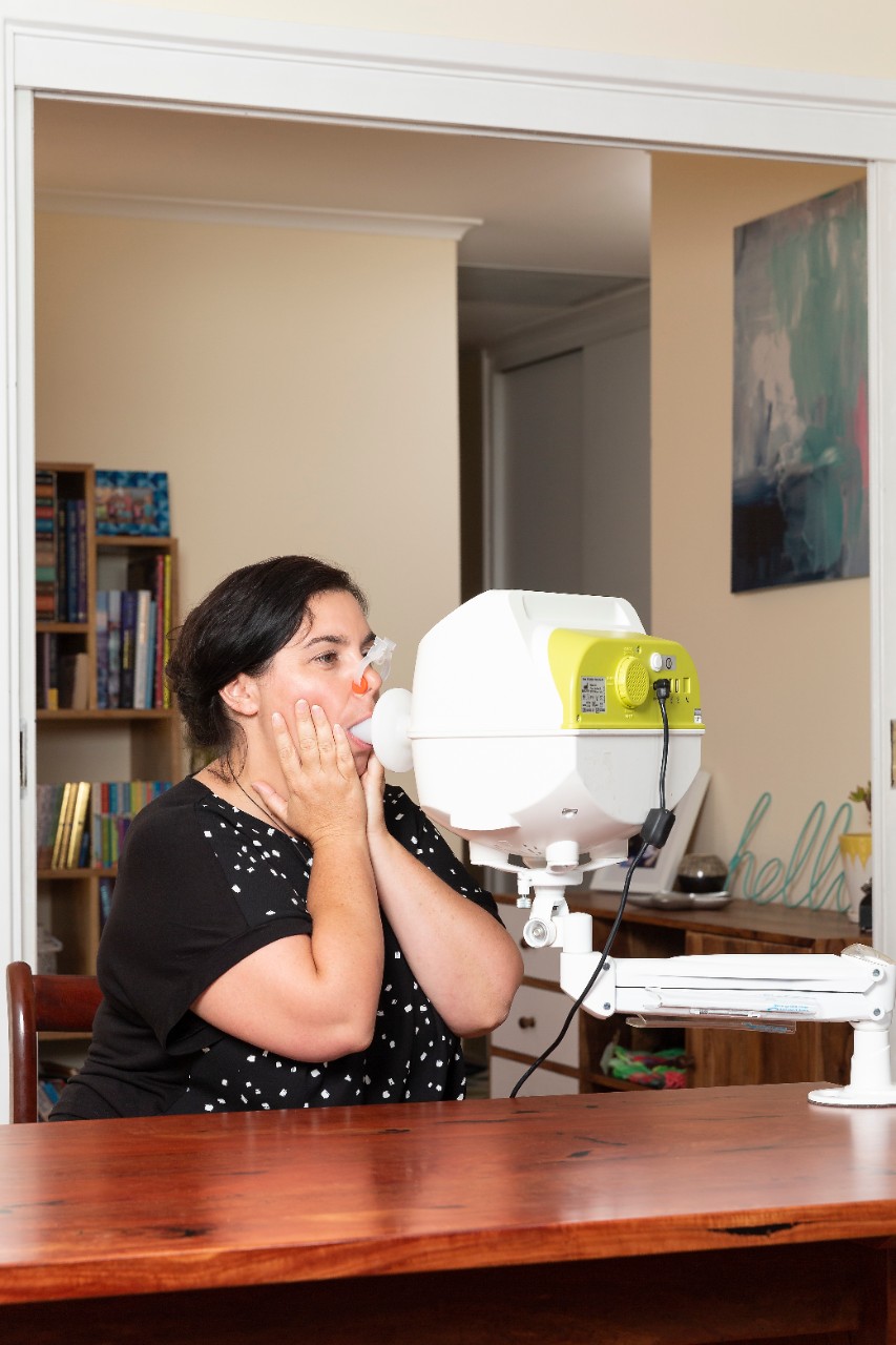 Photograph of Amy Webster using the use-at-home device to monitor lung function.