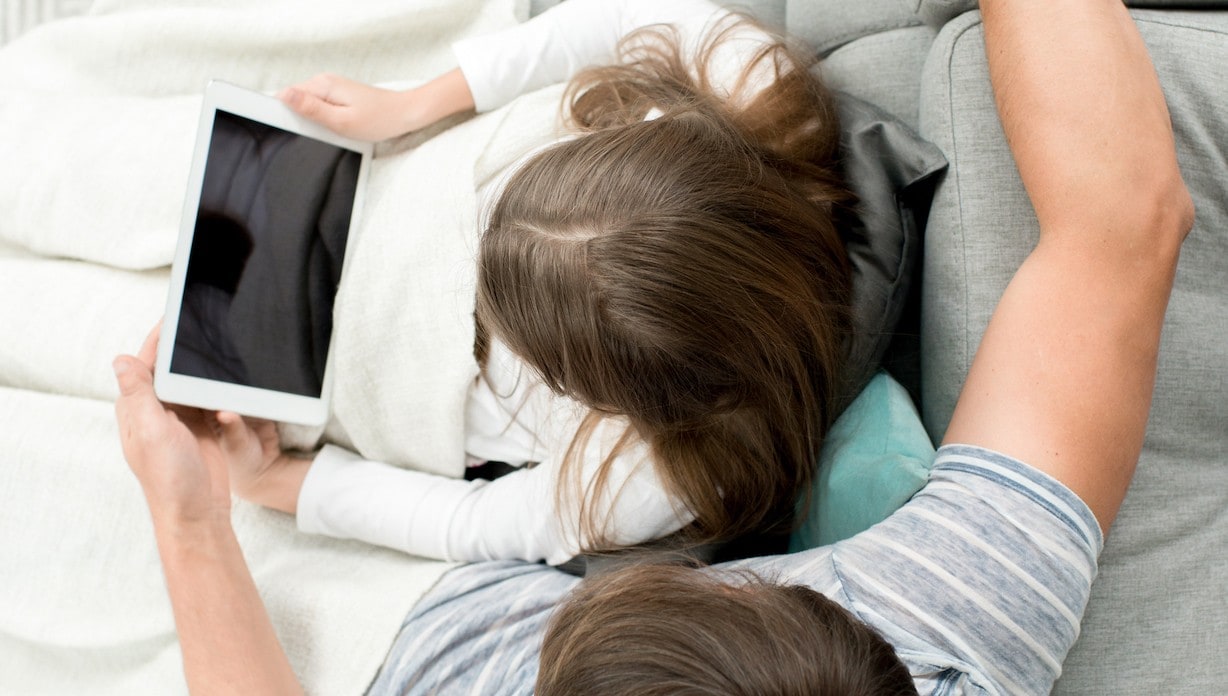 Child sitting with a parent, looking at a tablet.
