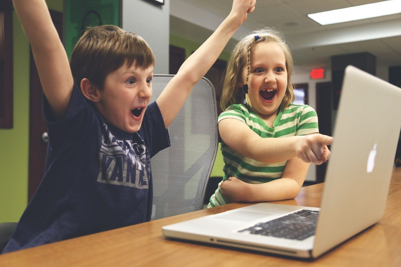 photo of two kids looking at a laptop, one of them is celebrating a win