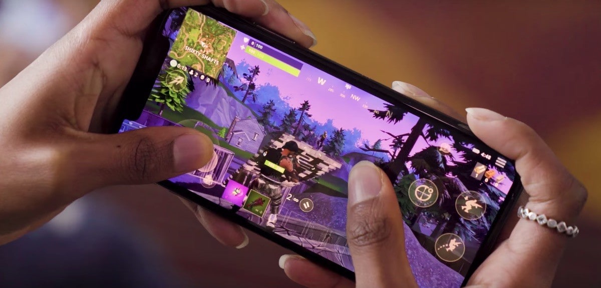 Photo of a woman's hands holding an iPhone and playing the game Fortnite