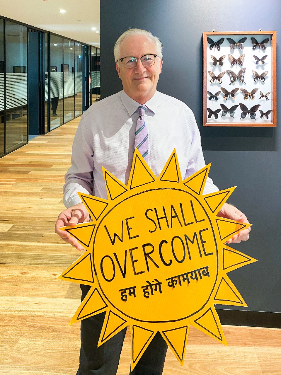 Vice-Chancellor Professor Stephen Garton holding a cut out yellow sun that says 'We shall overcome' in English and Hindi