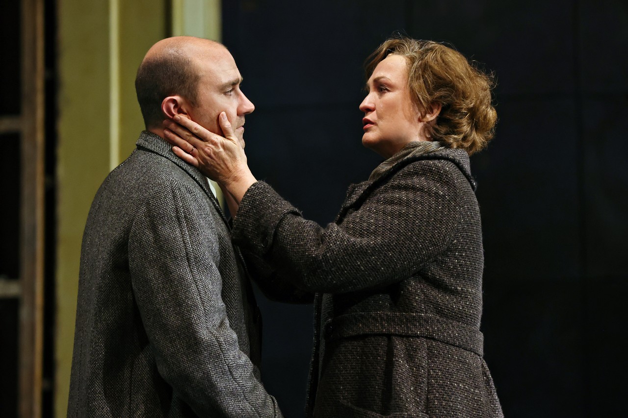 two actors on stage looking at each other, a woman is looking concerned and is touching the man's face