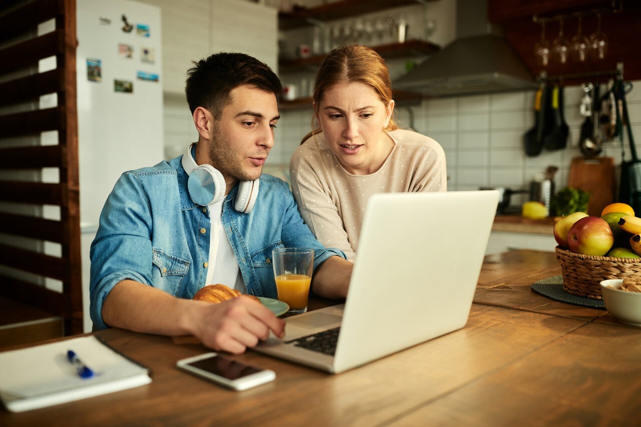photo of a woman and man looking at a laptop together in the kitchen.