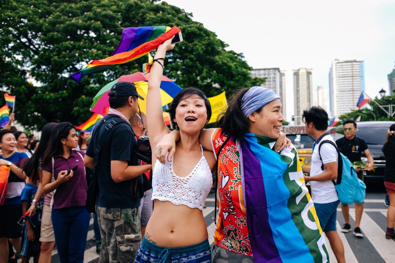 photo of two young women in Manila attending a Pride March with rainbow flags