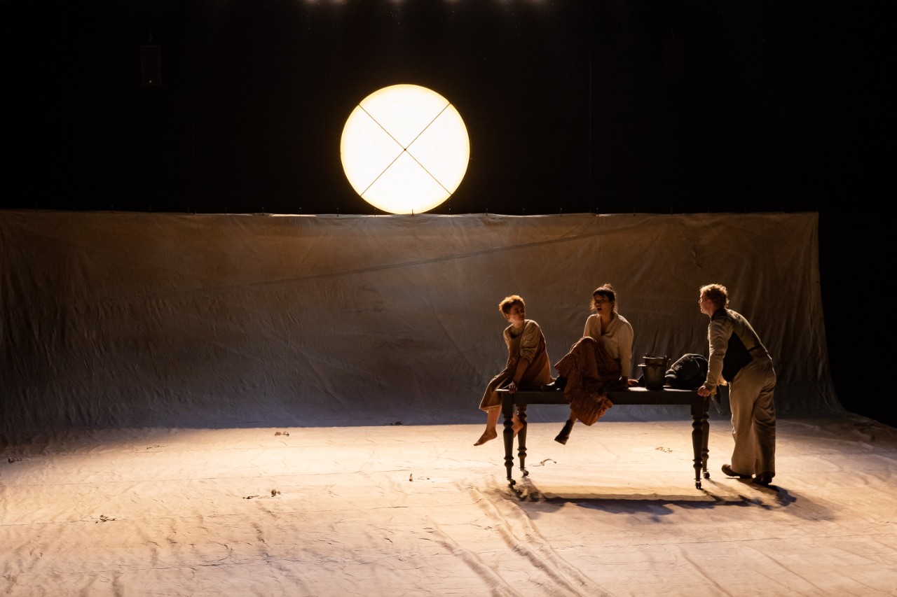 photo of three actors on stage with a large full moon above them