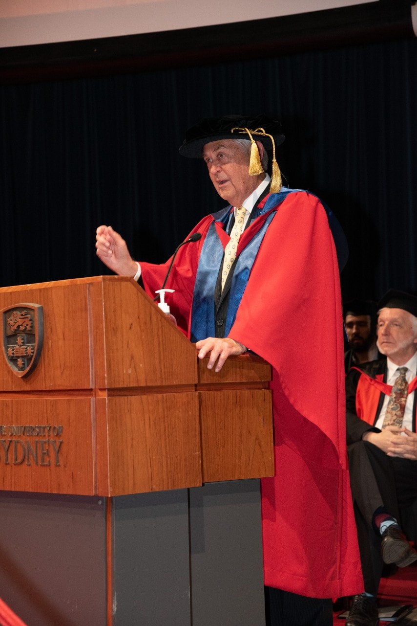 Chris Vonwiller at a lecturn, speaking after receiving his honorary doctorate, gesticulating with one arm.