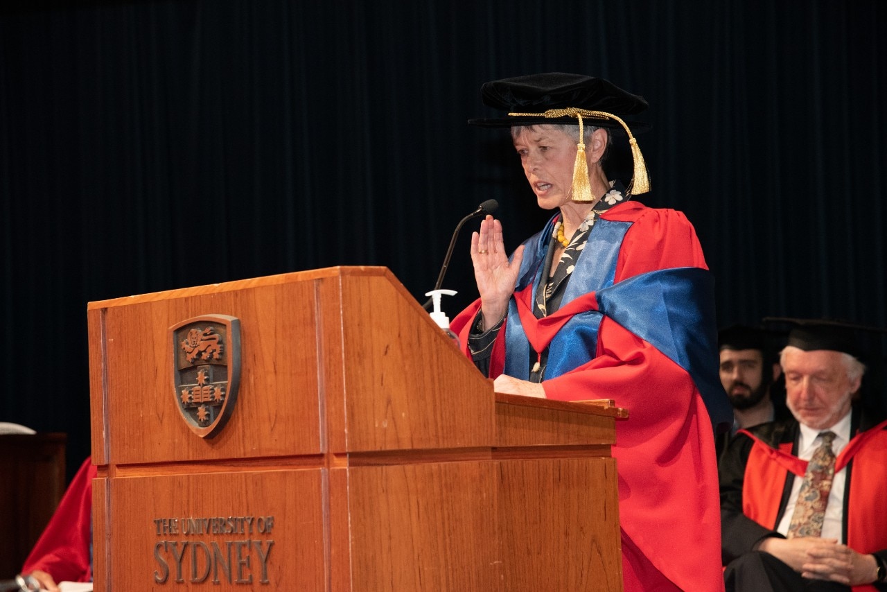 Julia Vonwiller at a lecturn delivering her address in graduation regalia after receiving her honorary doctorate. 