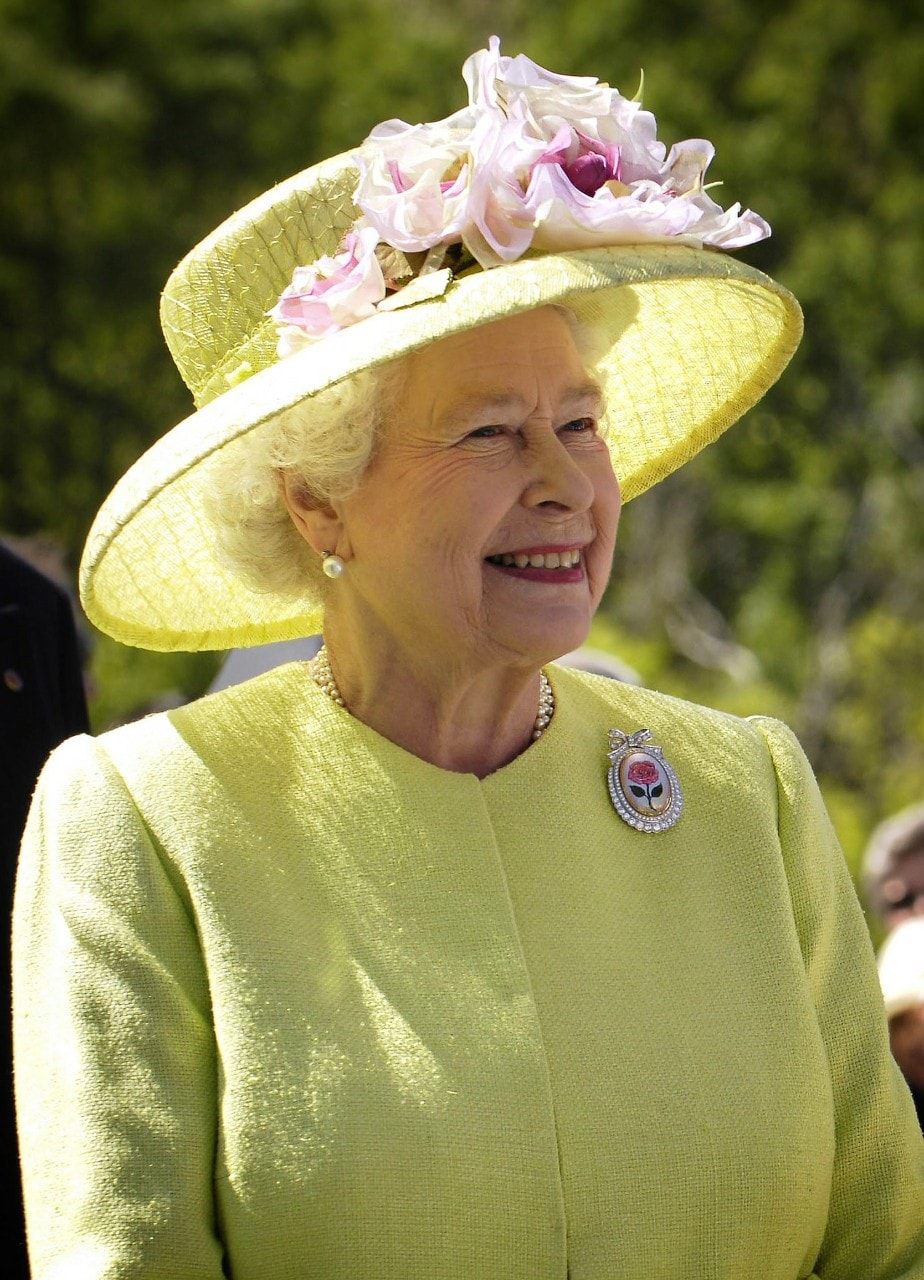 photo of an older Queen Elizabeth wearing a bright yellow dress and hat, smiling and waving at a crowd. 