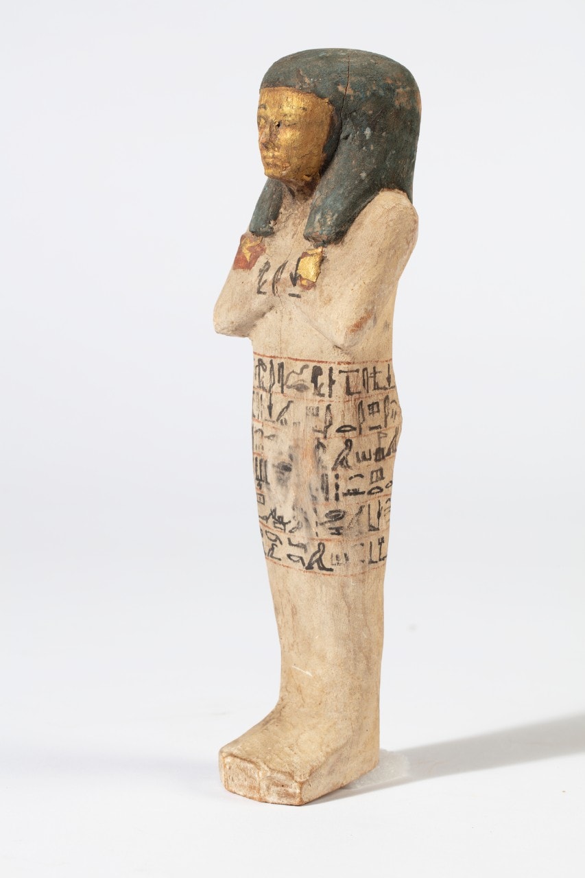 The shabti at an angle, its chest inscribed with hieroglyphs, against a light background. 