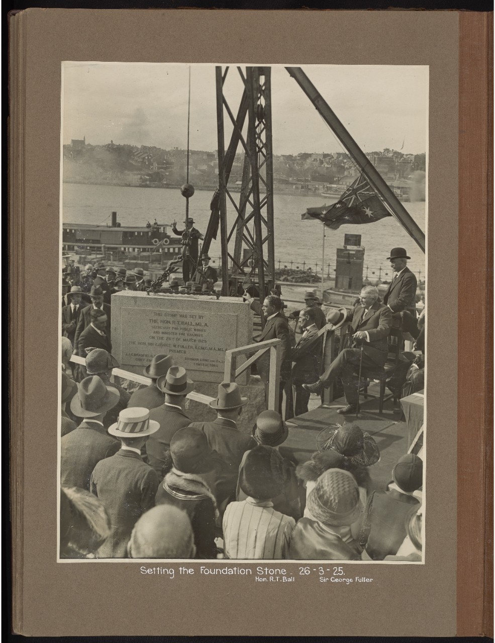 A page from an old photo album, featuring a black-and-white photograph of people gathered around a bridge's foundation stone.