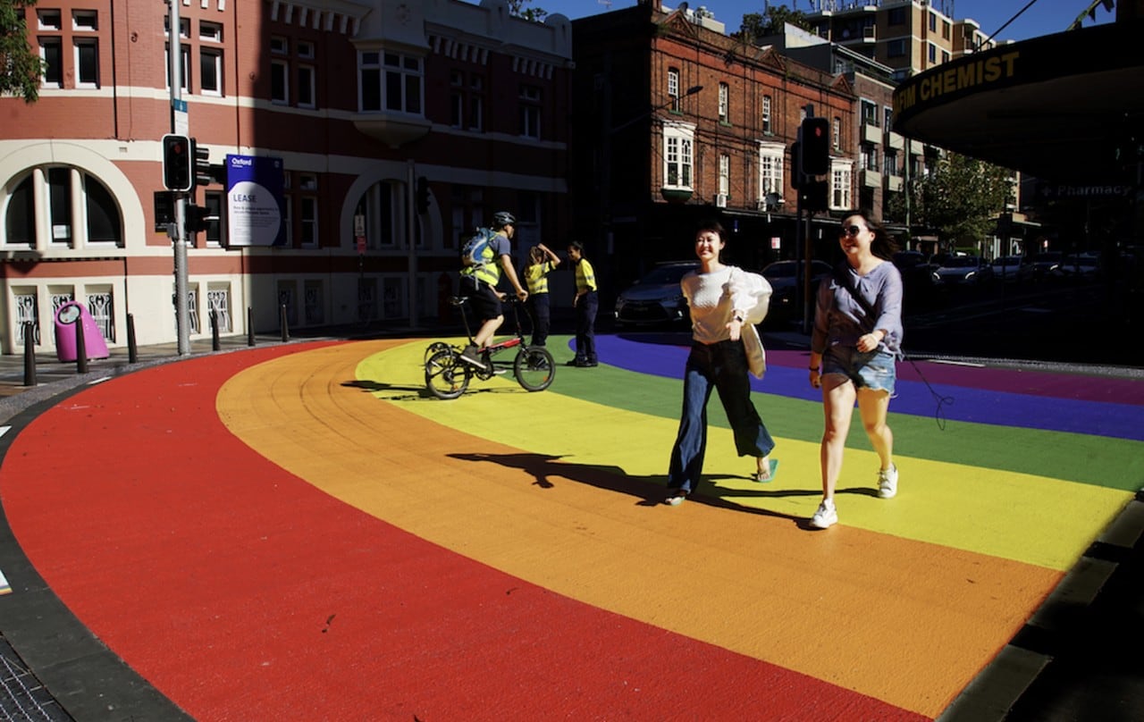 Two women on a rainbow pedestrian crossing.