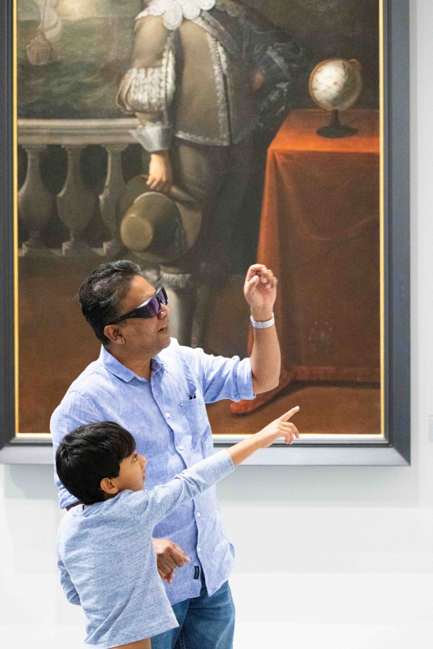 a father and son looking at a painting with glasses on to see brighter colours