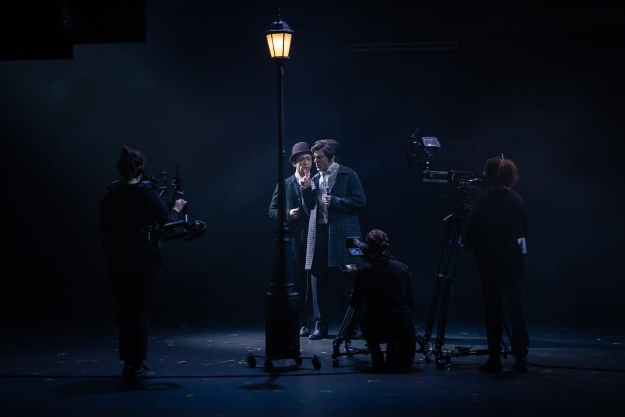 actors on a very dark stage under a London lamplight, three cameras are filming them