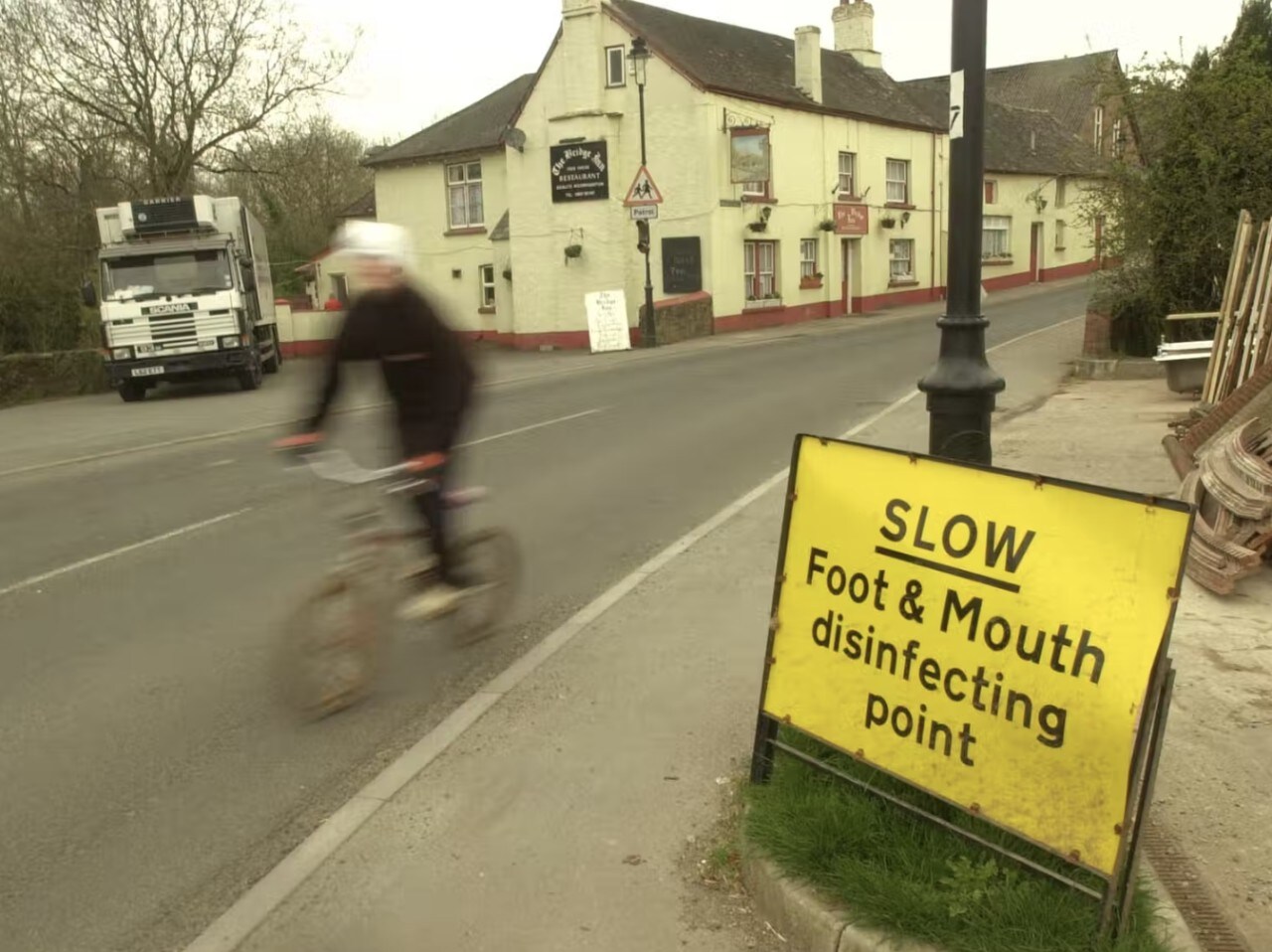 A cyclist next to a foot and mouth disease sign.