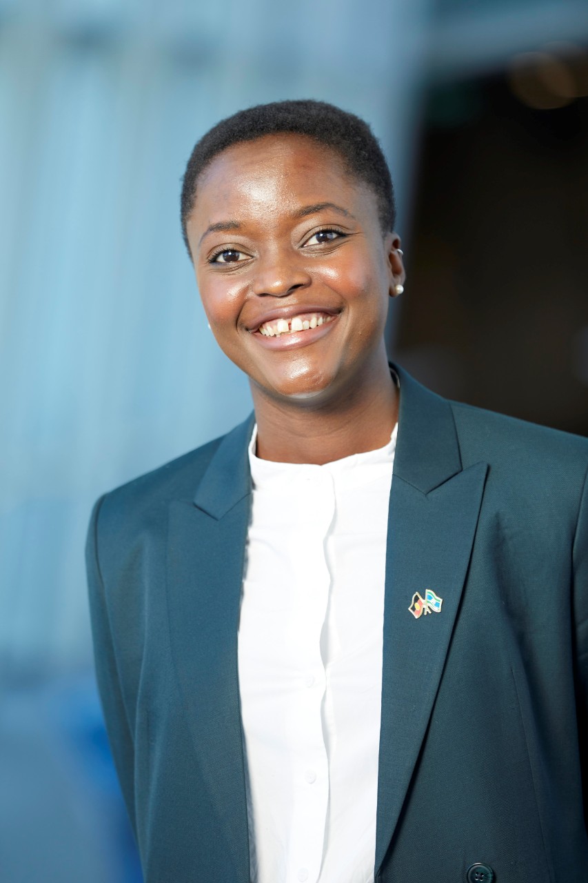 Woman with brown skin and short black hair smiling. She is wearing a teal blazer