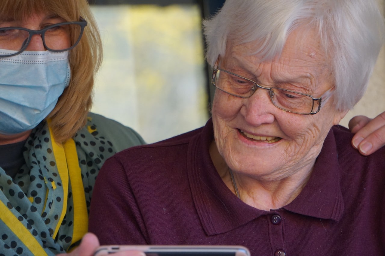 photo of a middle aged woman caring for an elderly woman looking at a mobile phone