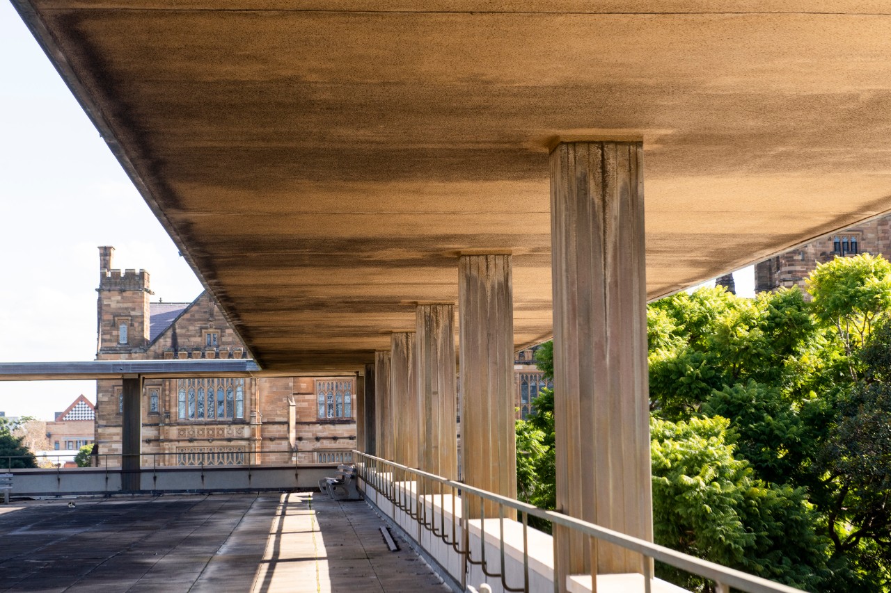 A photograph of a concrete terrace with views of treetops and sandstone buildings.