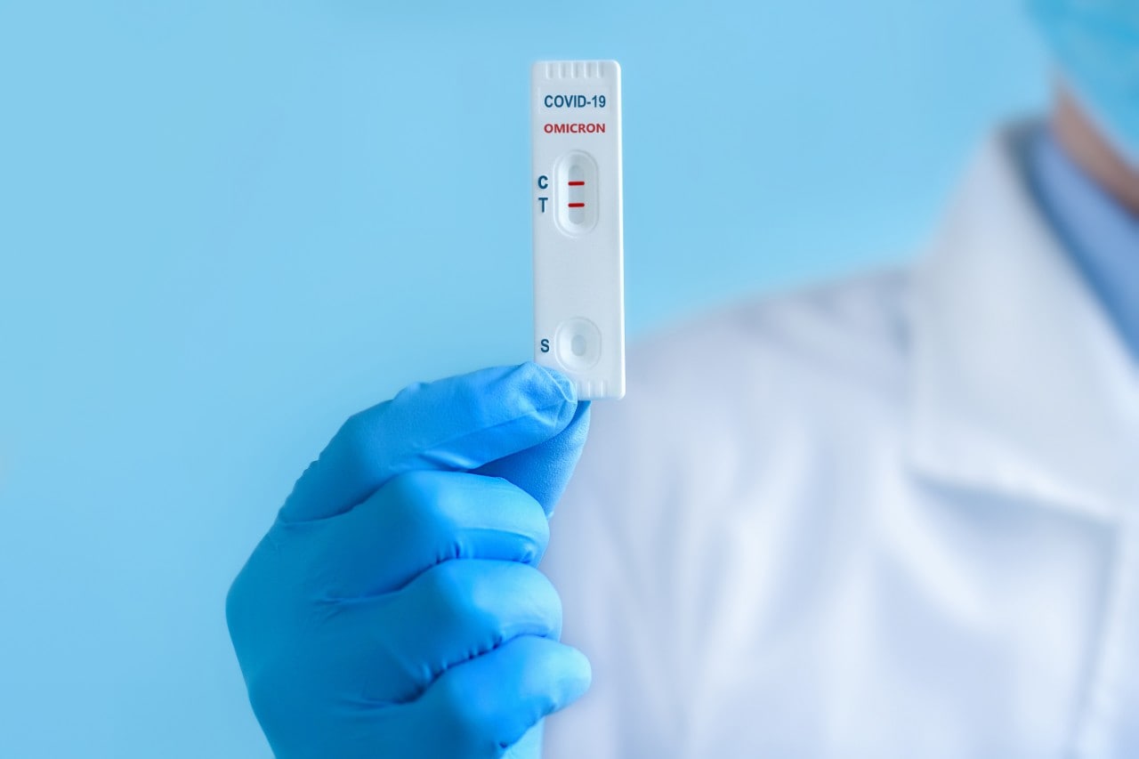 A rapid antigen test showing positive for COVID-19 held by a doctor in personal protective equipment.