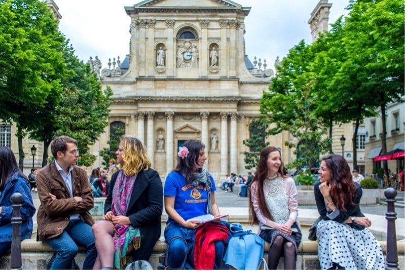 A photo of a group of young people sitting in front of a historic building
